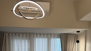 A hotel room with a large bed, a round ceiling light, a bedside table with a lamp, and sheer curtains.