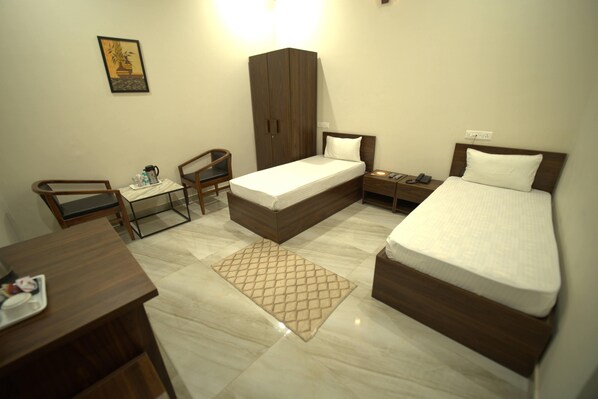 A compact hotel room with a single bed, a desk, a chair, a wardrobe, and a bedside table. - Hotel Omkar (Hisar)
