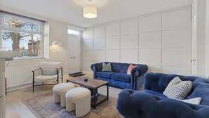 En moderne stue med en blå sofa, en hvid lænestol og skærmer, et sofabord og en gulvlampe.