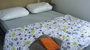 Un letto singolo con copriletto a pois, due cuscini e un asciugamano piegato. Sopra il letto, due mensole bianche.