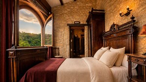 A bedroom with a large bed, a stone wall, a wooden headboard, and a view through an arched window. - Fortaleza Medieval La Manyosa (Granera)