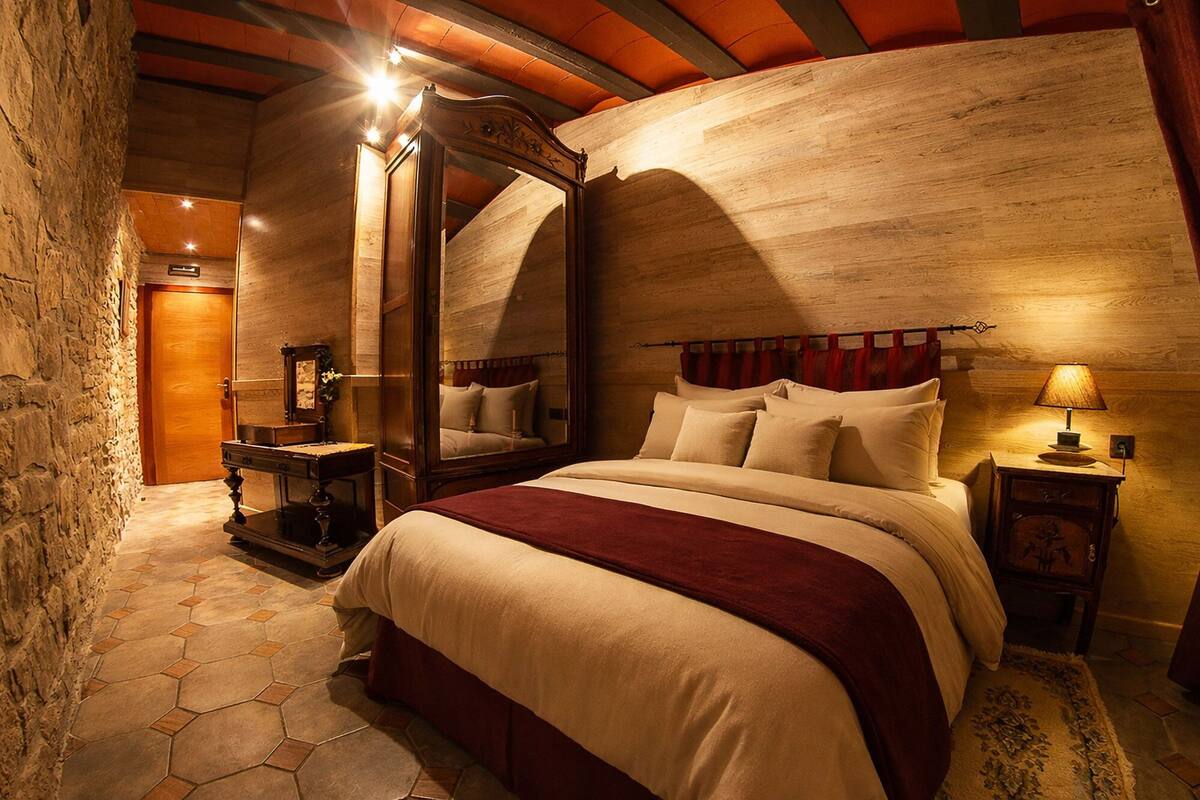 Ein Schlafzimmer mit einem großen Bett, einem Spiegel, einem Nachttisch und einer Steinwand.