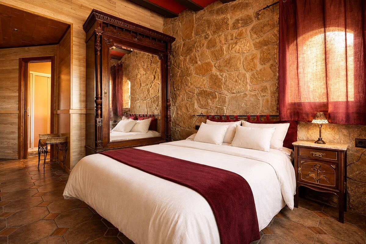 Ein Schlafzimmer mit Steinstruktur, einem großen Bett mit weißen Leinen, einem Holz-Kopfteil und einem Spiegel darüber.