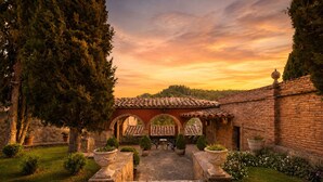 A courtyard with a brick wall, a tiled roof structure, and a stone pathway leading to an arched entrance. - Fortaleza Medieval La Manyosa (Granera)