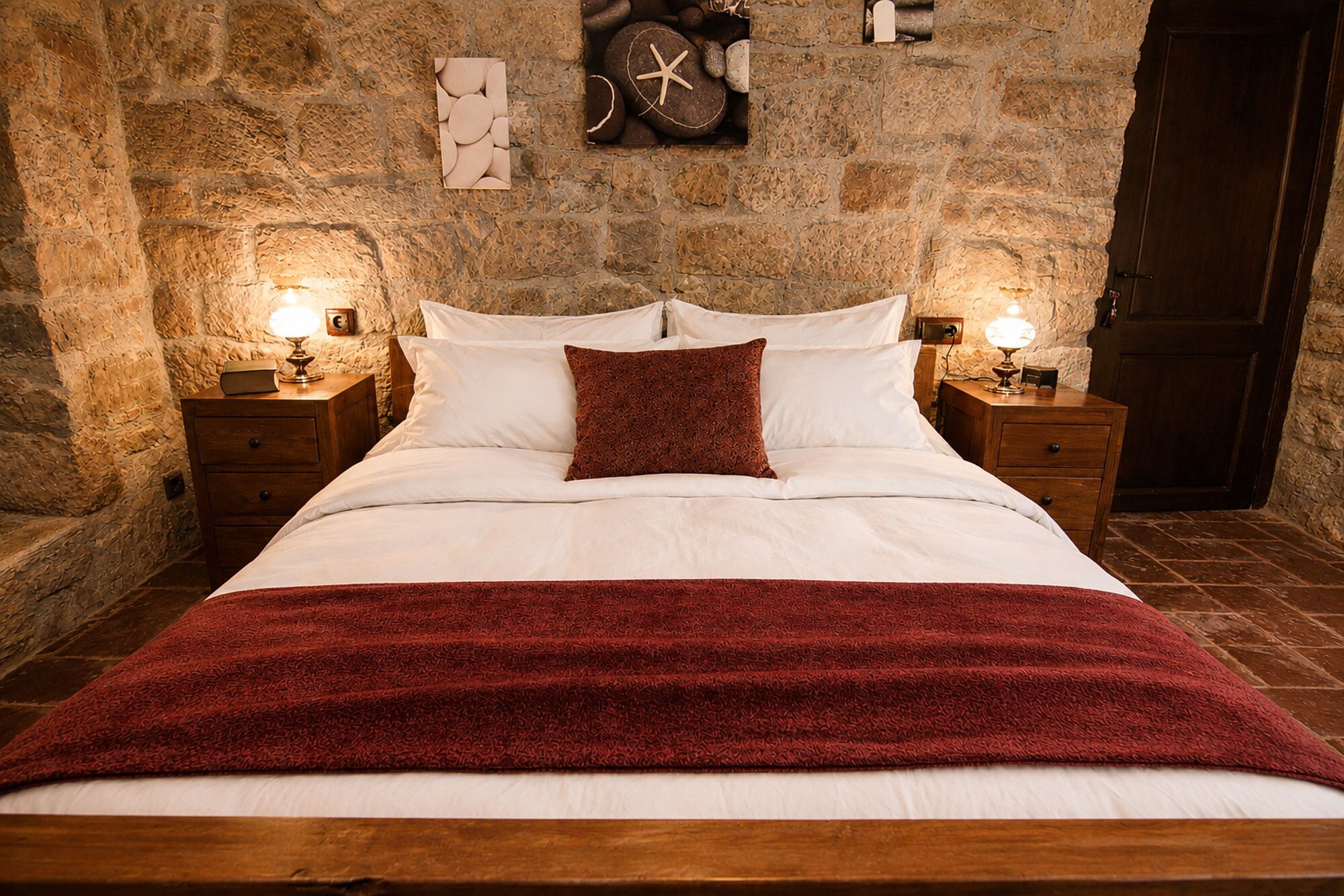 Un lit avec du linge de lit blanc, un plaid rouge et deux tables de chevet avec des lampes.