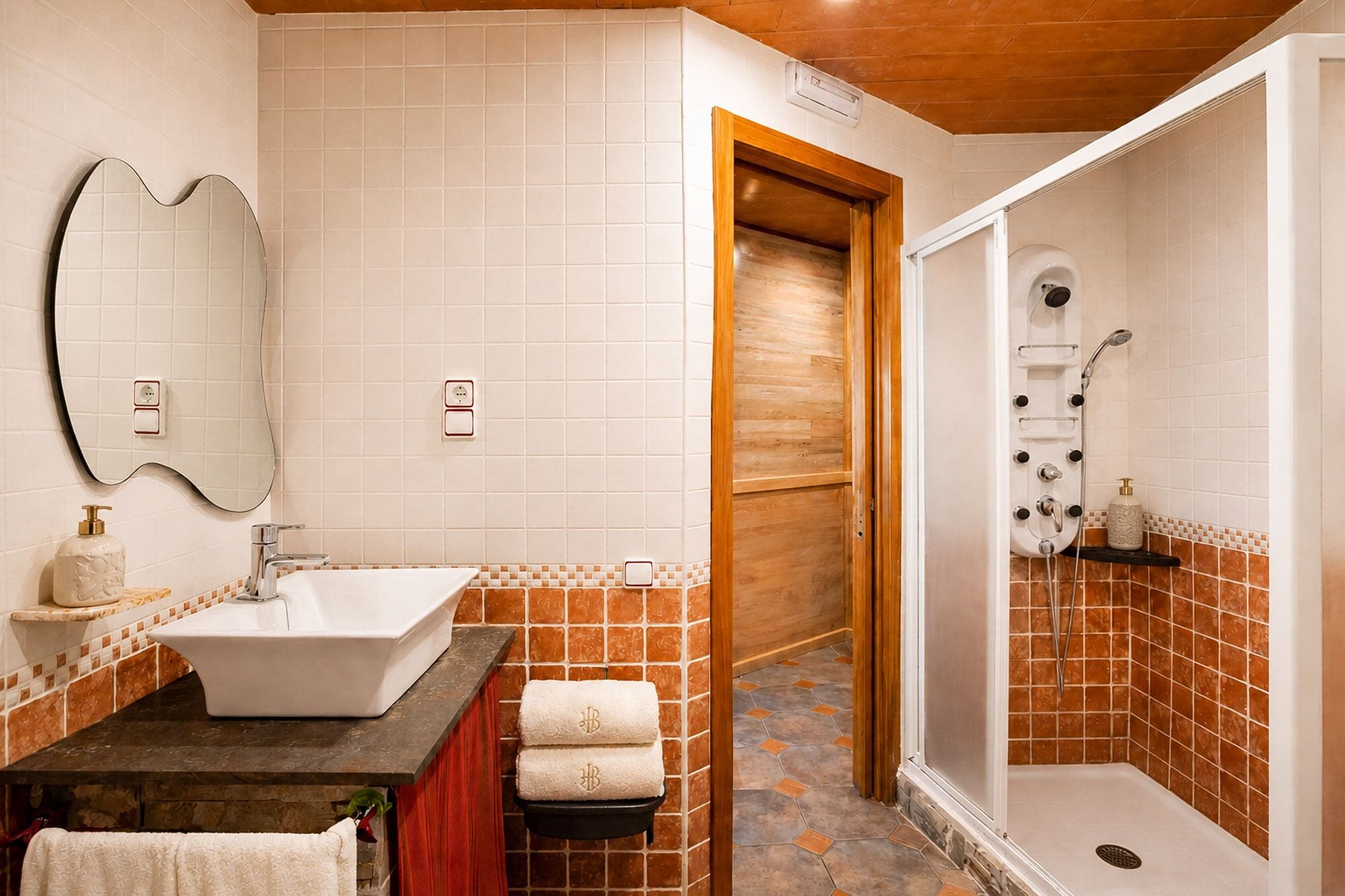 Une salle de bain avec un lavabo, un miroir, une douche et des murs carrelés.