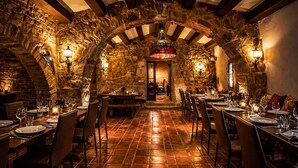 A restaurant with stone walls, wooden beams, and a central archway. Tables are set with plates and glasses. - Fortaleza Medieval La Manyosa (Granera)