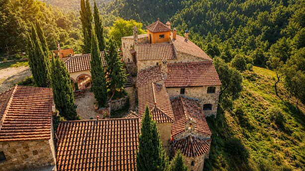 A traditional stone building with terracotta tiled roofs, surrounded by lush greenery and hills. - Fortaleza Medieval La Manyosa (Granera)