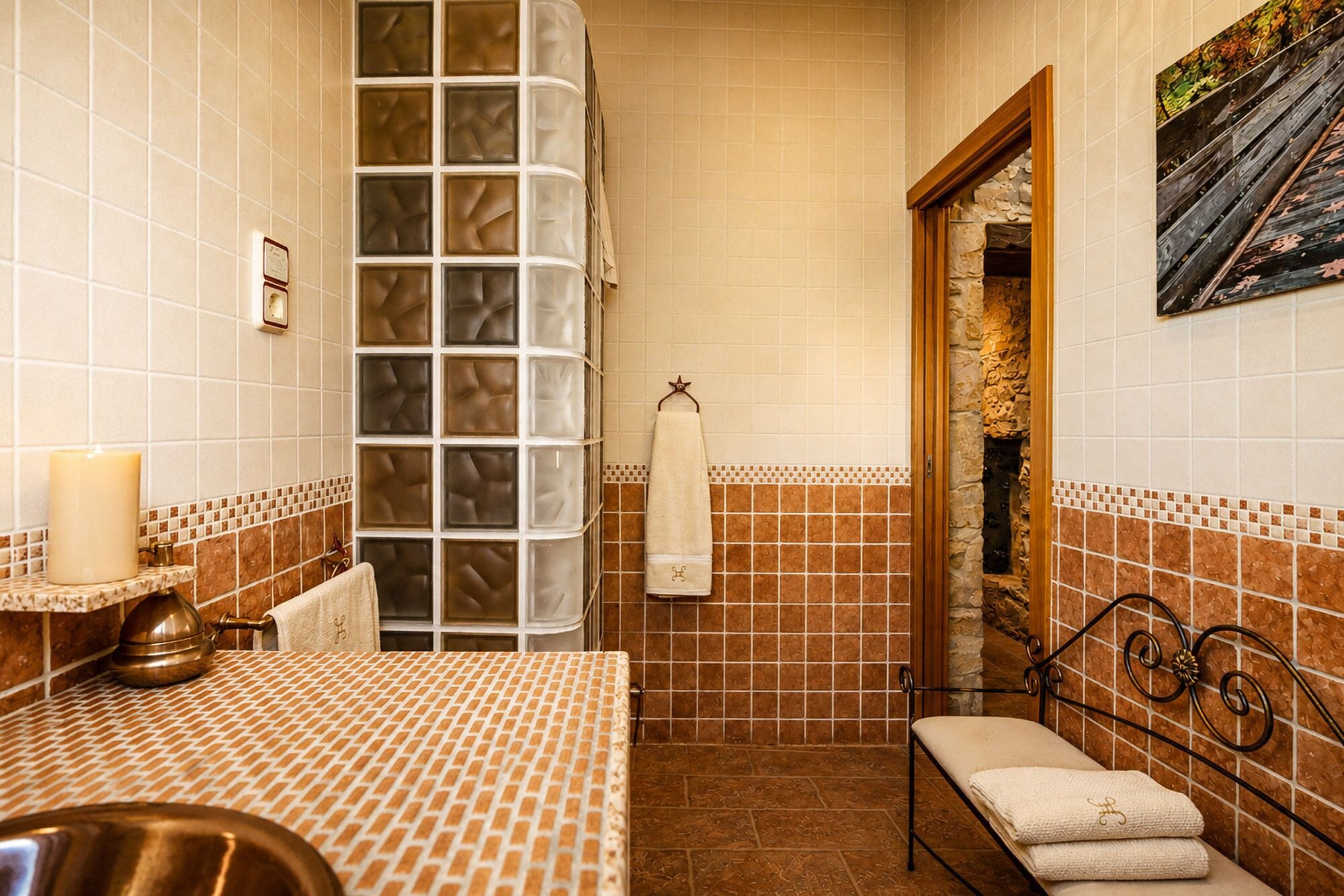 Un baño con pared de azulejos, un lavabo con encimera estampada, un perchero y un banco.