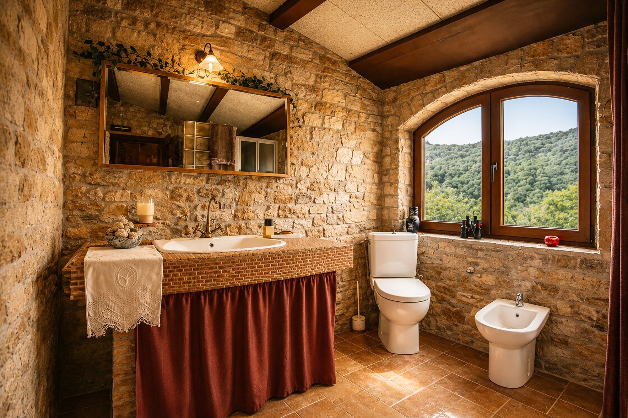 Un baño rústico con pared de piedra, tocador de madera, lavamanos, inodoro, bidé y ventana con vistas a la vegetación.