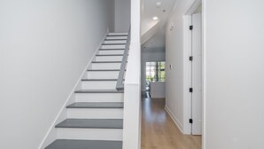 Una escalera de diseño moderno que conduce a un pasillo con piso de madera y paredes blancas.