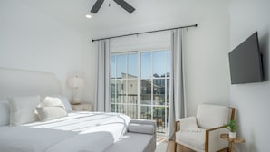 Un dormitorio moderno con una cama grande, una silla, un televisor y una ventana con cortinas.