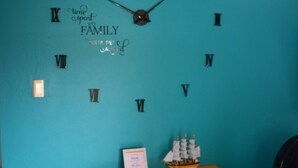 Una habitación con un gran reloj de pared que marca la hora, una pequeña mesa con un modelo de barco y un documento enmarcado sobre la mesa.