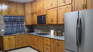 Una cocina con armarios de madera, un refrigerador de acero inoxidable, un microondas y una estufa a gas.