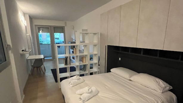 Una habitación de hotel moderna con una cama grande, un armario empotrado y una pequeña zona de escritorio.