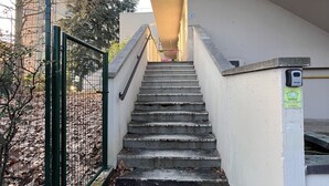 Una escalera que lleva a la entrada de un edificio, rodeada por una valla metálica y árboles.