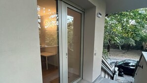 Un balcón con una puerta corredera de vidrio que da a una habitación, un felpudo y un coche estacionado afuera.