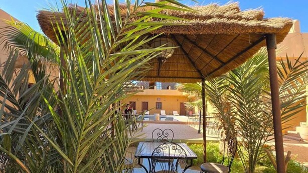 An outdoor seating area with a thatched roof, a tiled floor, and palm trees. - nomad apartments (Taouz)
