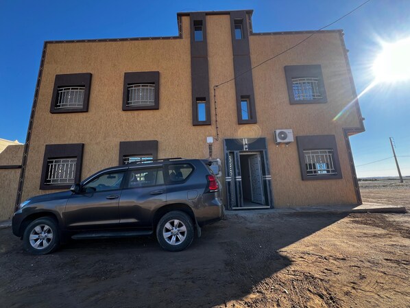A building with multiple windows and a door, a parked car in front, and an air conditioning unit on the wall. - nomad apartments (Taouz)