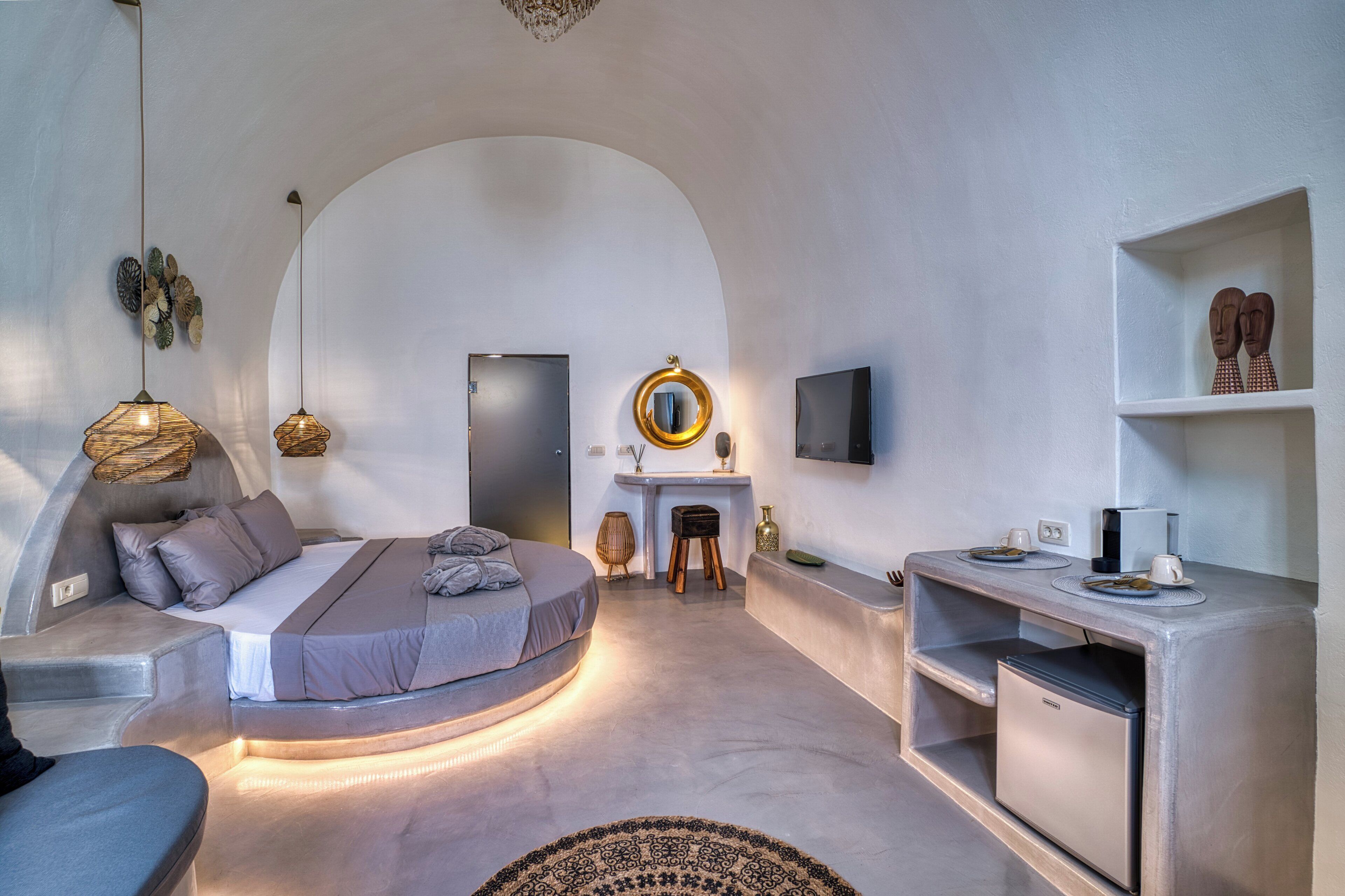 Een moderne slaapkamer met een gebogen bed, een klein bureau, een televisie en een geïntegreerde minibar.