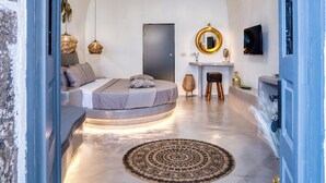 A modern bedroom with a curved ceiling, a bed with a headboard, a round rug, and a chandelier. - 360o 2BD Panoramic Apartment (Santorini)