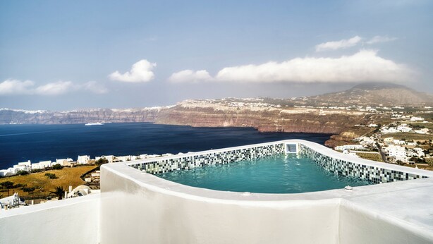 A pool with a tiled edge, overlooking a coastal town and cliffs. - 360o 2BD Panoramic Apartment (Santorini)