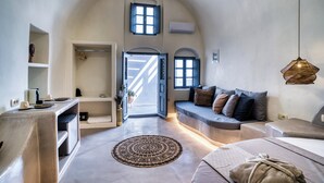 A spacious room with a high arched ceiling, a seating area with cushions, a round patterned rug, and a hanging light fixture. - 360o 2BD Panoramic Apartment (Santorini)