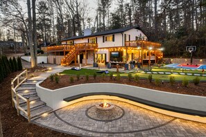 A two-story house with a deck, outdoor seating, a fire pit, and a basketball court. - Stunning 5BR w/ Hot Tub, Sauna, Firepit & Theater | 20 Mins to Asheville|*New* (Arden)