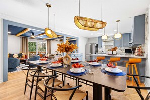 A modern kitchen with a central island, pendant lighting, and a dining area with a long table set for six. - Stunning 5BR w/ Hot Tub, Sauna, Firepit & Theater | 20 Mins to Asheville|*New* (Arden)