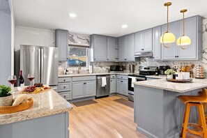 A modern kitchen with grey cabinets, stainless steel appliances, a marble backsplash, and a central island with bar stools. - Stunning 5BR w/ Hot Tub, Sauna, Firepit & Theater | 20 Mins to Asheville|*New* (Arden)
