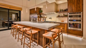 Une cuisine moderne dotée d’un îlot central, de tabourets de bar, de meubles en bois et d’appareils électroménagers intégrés.