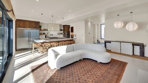 Un salon moderne doté d’un grand canapé d’angle, d’un espace cuisine avec un îlot central et d’un coin repas avec des tabourets de bar.