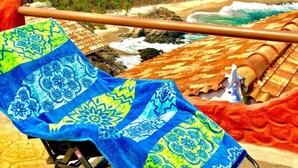 A beach view with a chair covered in a blue and yellow patterned towel, a wooden railing, and a thatched-roof structure in the background. - BUNGALOW POOL AND SEMI-PRIVATE BEACH, ZIPOLITE-MAZUNTE BEACH, 8 NEARBY BEACHES (San Pedro Pochutla)