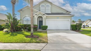 A single-story house with a garage, surrounded by well-maintained landscaping including palm trees and shrubs.