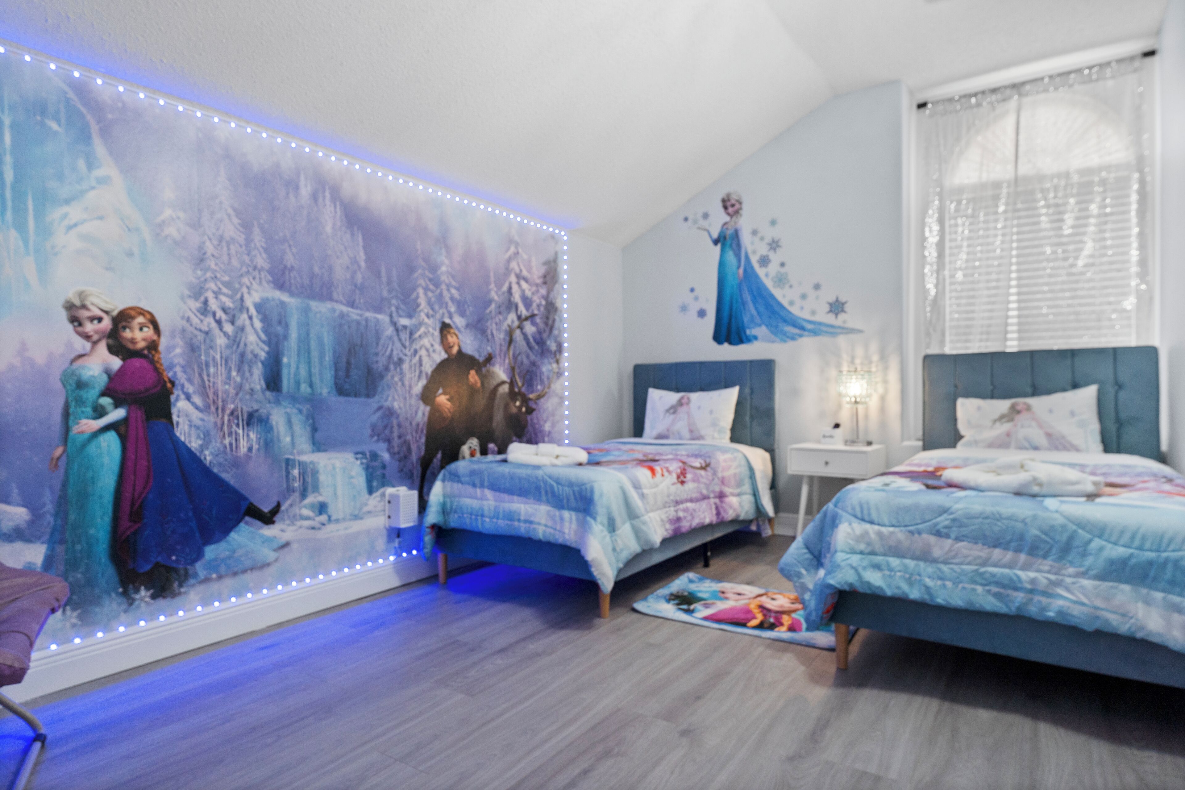 A bedroom with two beds, a large wall mural, and LED strip lighting.