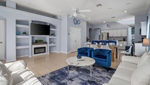 Una sala de estar moderna con chimenea, televisor y comedor con sillas azules.