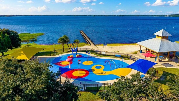 A colorful playground with a water slide and a gazebo by the water.