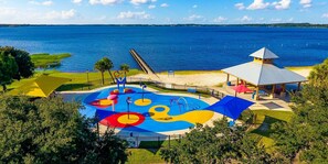 Een kleurrijk speelterrein met een glijbaan en een tuinhuisje aan het water.