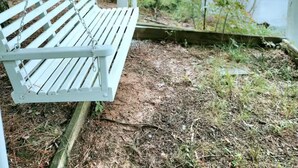 Una sedia a dondolo in legno bianco sospesa su un portico coperto con vista su un lago.