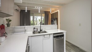 Une cuisine moderne avec des meubles blancs, un lave-vaisselle encastré, une fenêtre avec des rideaux et une plante en pot posée sur le rebord de la fenêtre.
