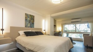 Une chambre d’hôtel moderne avec un grand lit, des tables de chevet, un bureau et une fenêtre donnant sur la verdure.