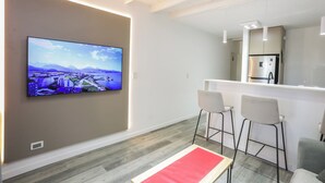 Une cuisine moderne avec un réfrigérateur en acier inoxydable, un plan de travail blanc et des tabourets de bar.