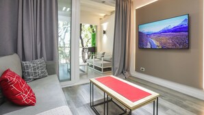 Un salon moderne avec un canapé, un coussin rouge, une table et un grand téléviseur fixé au mur.