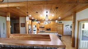A kitchen with wooden cabinets, a central island with stools, and pendant lighting. - Spacious Retreat on Caddo River, Amity (Amity)