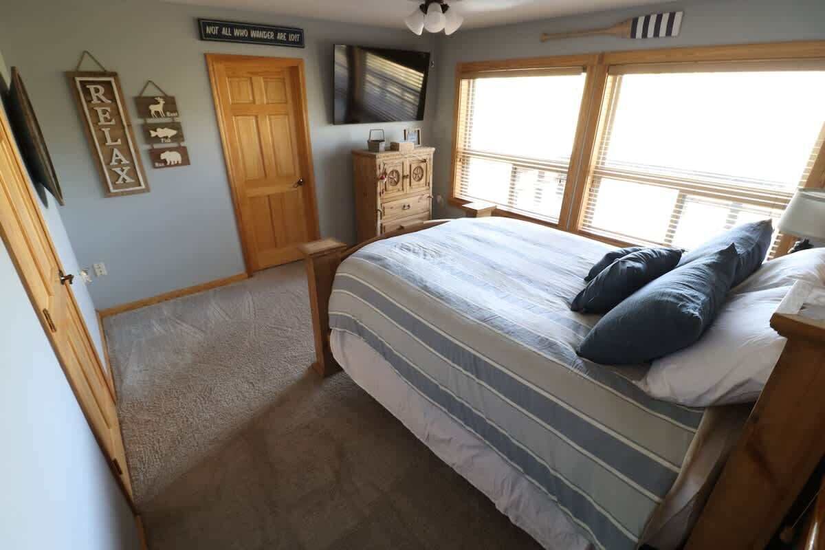A bedroom with a bed, a dresser, a television, and a window with blinds.