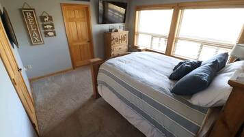 A bedroom with a bed, a dresser, a television, and a window with blinds.