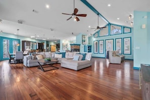 A spacious living room with a wooden floor, a sectional sofa, a dining area, and a kitchen in the background.
