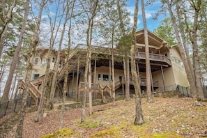 A cabin with a wooden deck, multiple staircases, and a stone foundation surrounded by trees.