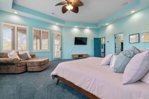 A bedroom with a bed, a sofa, a ceiling fan, a TV, and a door.
