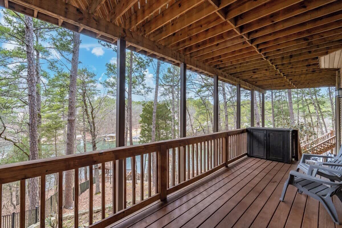Una terraza de madera con barandilla, un área de estar con sillas y vistas a un bosque.